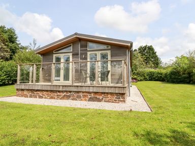 A wooden cabin with glass doors and a small deck with two chairs and a table in a grassy yard at 6 Southern Place in Dobwalls