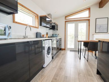 A kitchen with black cabinets a washing machine a dining table and chairs at 6 Southern Place in Dobwalls