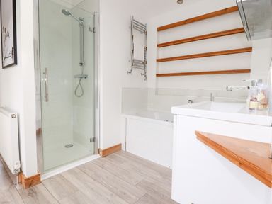 A bathroom with a glass shower enclosure bathtub wooden shelves and white sink at 6 Southern Place in Dobwalls