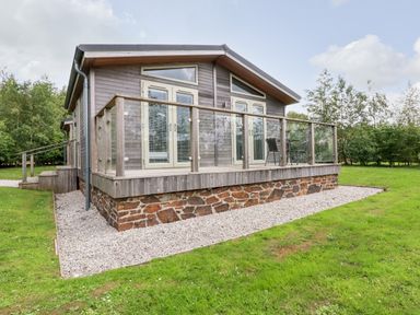 A small wooden house with glass doors and a balcony with chairs on grass at 6 Southern Place in Dobwalls