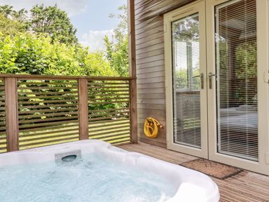 An outdoor hot tub on a wooden deck next to glass doors with blinds at 6 Southern Place in Dobwalls