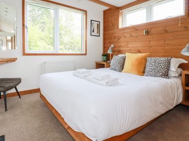 A bedroom with a double bed white bedding and folded towels on it wooden wall paneling and windows at 6 Southern Place in Dobwalls