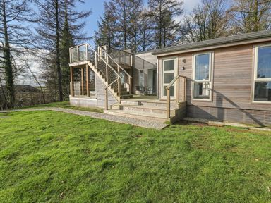 A wooden house with a deck and stairs surrounded by grass and trees at 4 Faraway Fields in Dobwalls