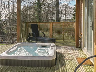An outdoor wooden deck with a hot tub black lounge chair and sliding glass door at 4 Faraway Fields Dobwalls