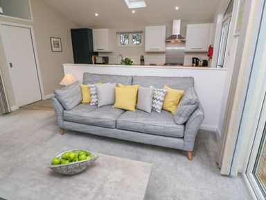 A living room with a grey sofa and yellow and grey pillows a coffee table with green apples and a kitchen in background at 4 Faraway Fields Dobwalls
