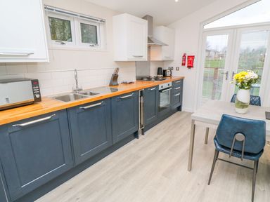 A kitchen with blue cabinets wooden countertop dining table with flowers and blue chairs at 4 Faraway Fields in Dobwalls