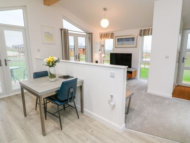 A dining area with a table and chairs next to a living room with a TV and floor lamp at 4 Faraway Fields in Dobwalls