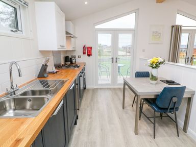 A kitchen with wooden countertops blue cabinets a dining table with flowers and chairs at 4 Faraway Fields in Dobwalls
