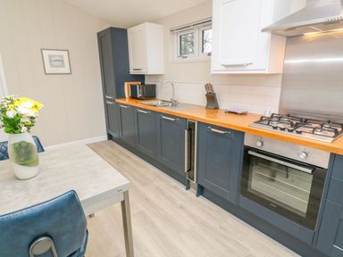 A kitchen with blue and white cabinets a wooden countertop a gas stove oven microwave and dining table with flowers at 4 Faraway Fields in Dobwalls