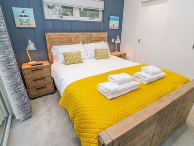 A bedroom with a wooden bed frame a yellow bedspread white towels on the bed two bedside tables with lamps and paintings on the blue wall at 4 Faraway Fields in Dobwalls