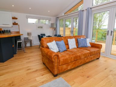 A living room with a brown sofa with pillows and a dining area with chairs near large glass doors at 21 Meadow Retreat in Dobwalls
