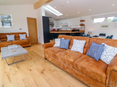 A living room with two brown sofas with cushions a coffee table and an open kitchen area at 21 Meadow Retreat in Dobwalls
