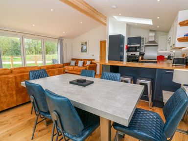 An open-plan living area with a dining table and blue chairs a kitchen with dark cabinets and wooden countertop and brown sofas near glass doors at 21 Meadow Retreat in Dobwalls