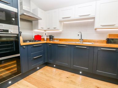 A kitchen with blue lower cabinets and white upper cabinets wooden countertops a gas stove a built in oven and microwave a stainless steel sink and wooden floor at 21 Meadow Retreat in Dobwalls