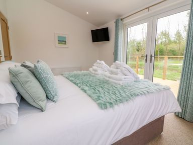 A bedroom with a bed pillows folded towels a wall-mounted tv and glass doors with curtains at 21 Meadow Retreat Dobwalls