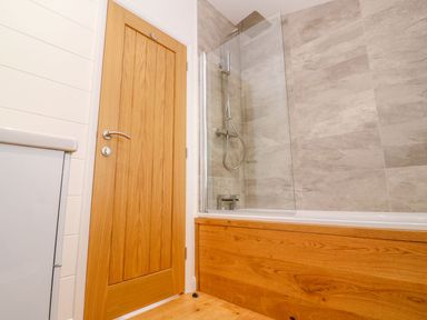 A bathroom with a wooden door a bathtub with a wooden panel and tiled walls at 21 Meadow Retreat in Dobwalls