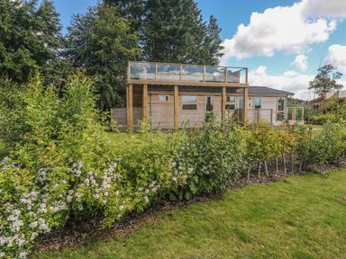 A wooden house with a glass balcony and garden with flowering shrubs at 2 Southern Place in Dobwalls