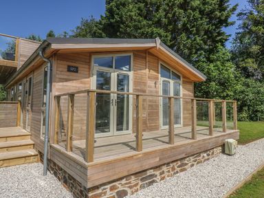 A wooden cabin with glass doors and a glass railing deck surrounded by gravel and trees at 2 Southern Place in Dobwalls