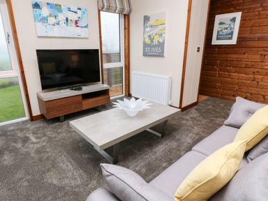 A living room with a television on a wooden stand a gray coffee table with a decorative item and a gray sofa with yellow cushions at 2 Southern Place in Dobwalls