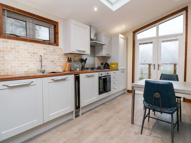 A kitchen with white cabinets wooden countertop dining table and blue chairs at 2 Southern Place in Dobwalls