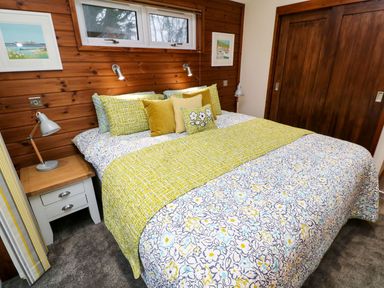 A bedroom with a bed covered in floral and patterned bedding next to a nightstand with a lamp and wood panel wall at 2 Southern Place in Dobwalls