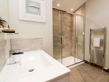 A bathroom with a sink and faucet a glass shower enclosure and a chrome towel radiator at 2 Southern Place in Dobwalls