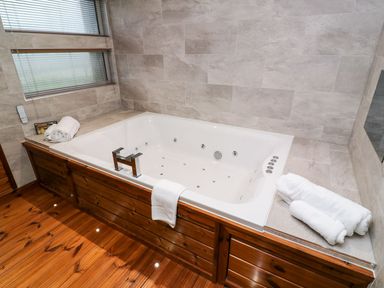 A bathroom with a white bathtub with wooden paneling towels on the tub edge and gray tiled walls at 2 Southern Place in Dobwalls