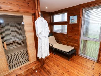 A wooden sauna room with a reclining chair a white robe hanging on the wall and windows with blinds at 2 Southern Place in Dobwalls