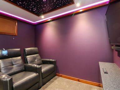 A small home theater room with two black leather recliners a wall mounted television and purple walls at 2 Southern Place in Dobwalls