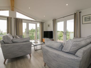 A living room with two gray sofas a coffee table a TV on a wooden stand and large windows at 7 Faraway Fields in Dobwalls