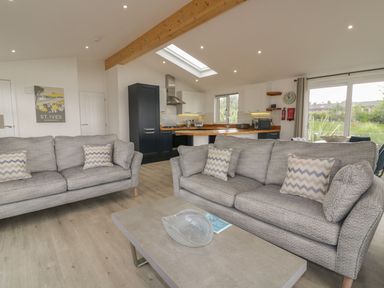 A living room with two gray sofas facing a coffee table and an open kitchen with wooden counters and cabinets at 7 Faraway Fields Dobwalls