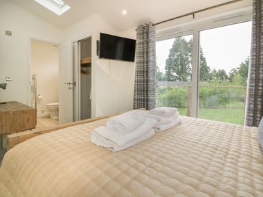 A bedroom with a bed and folded towels on it a wall mounted tv an open door showing a toilet and a window with curtains and a view of trees at 7 Faraway Fields in Dobwalls