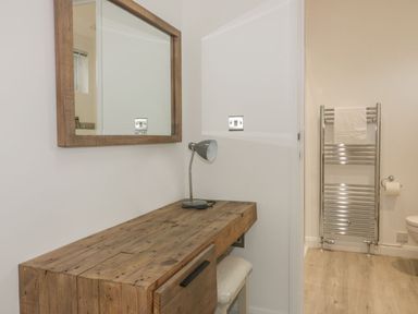A wooden dressing table with a small lamp and a mirror above it next to a heated towel rail in a bathroom at 7 Faraway Fields in Dobwalls