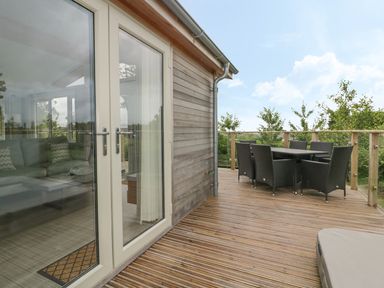 An outdoor wooden deck with a black dining table and chairs next to glass doors at 7 Faraway Fields in Dobwalls