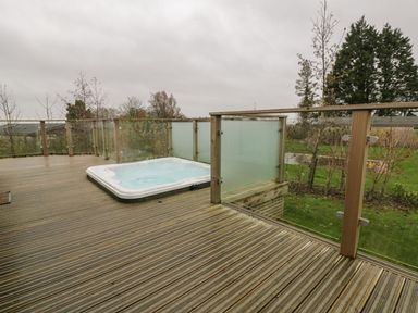 An outdoor deck with a hot tub and glass railings overlooking a garden at 7 Faraway Fields in Dobwalls