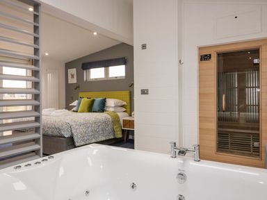 A bedroom with a bed and pillows next to a white bathtub and a wooden sauna door at 19 Meadow Retreat in Dobwalls