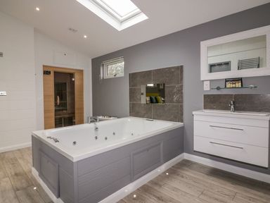 A bathroom with a large bathtub, a wall-mounted sink with a mirror, a small window, a skylight, and a wooden sauna at 19 Meadow Retreat in Dobwalls
