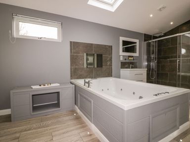 A bathroom with a large bathtub a vanity with a mirror a shower with glass doors and a small window at 19 Meadow Retreat in Dobwalls