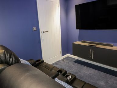 A room with a black leather sofa, a wall-mounted TV, a white door, and a gray cabinet with a soundbar and remote at 19 Meadow Retreat in Dobwalls