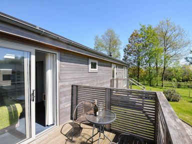 A balcony with a glass table and two chairs outside a wooden house with trees in the background at 19 Meadow Retreat in Dobwalls