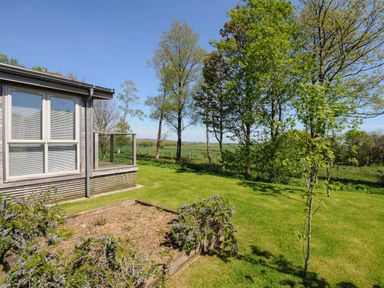 A garden with trees and grass next to a house with large windows at 19 Meadow Retreat in Dobwalls