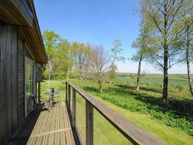 A wooden balcony with a table and two chairs overlooking a grassy area and trees at 19 Meadow Retreat in Dobwalls