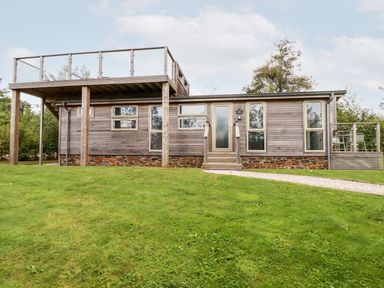 A single story wooden house with a deck and rooftop terrace on a grassy lawn at 1 Southern Place in Dobwalls