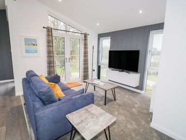 A living room with a blue sofa yellow cushions coffee table TV on wall unit and patio doors at 1 Southern Place in Dobwalls
