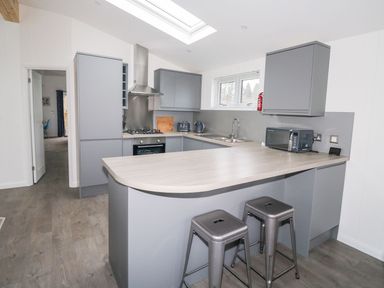 A kitchen with grey cabinets a stove a microwave and two metal stools at 1 Southern Place in Dobwalls