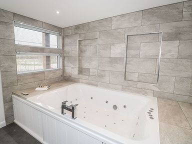 A bathroom with a large white jacuzzi tub and tiled walls with windows at 1 Southern Place in Dobwalls