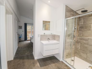 A bathroom with a shower enclosure and a wall-mounted sink next to a hallway leading to a bedroom with a blue chair at 1 Southern Place in Dobwalls