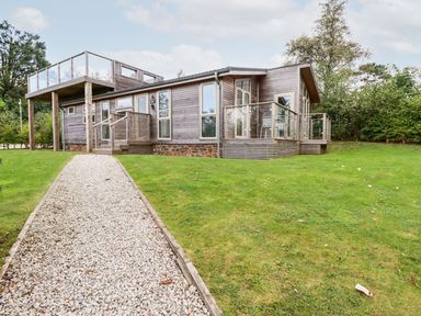 A modern wooden house with glass railings and a gravel pathway on a grassy lawn at 1 Southern Place in Dobwalls