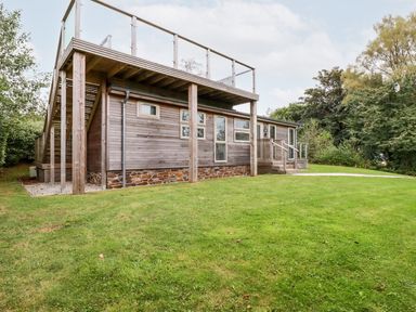 A wooden house with multiple windows and an upper deck on a grassy lawn surrounded by trees at 1 Southern Place in Dobwalls