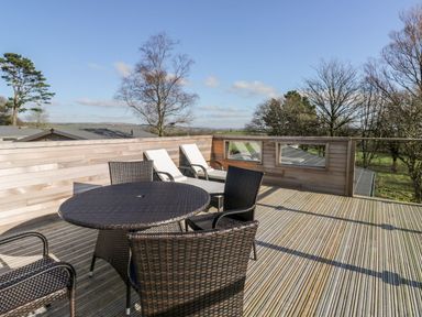 An outdoor deck with a round table, four wicker chairs, and two white lounge chairs at 1 Southern Place in Dobwalls